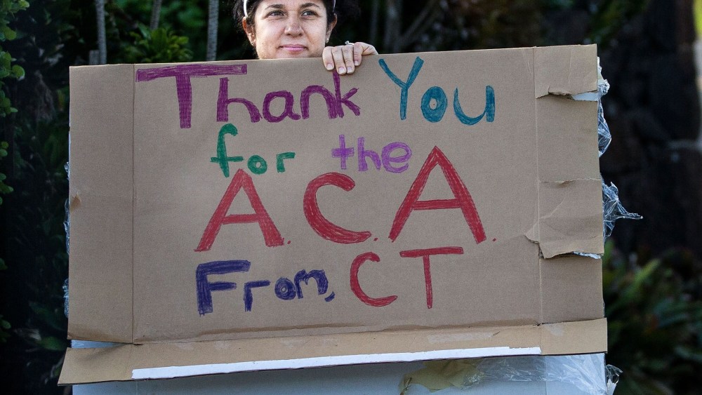A woman holding a sign in support of the Affordable Care Act is seen as President Barack Obama's motorcade returns to his vacation compound from the gym at Marine Corps Base Hawaii on December 29, 2013 in Kaneohe Bay, Hawaii.