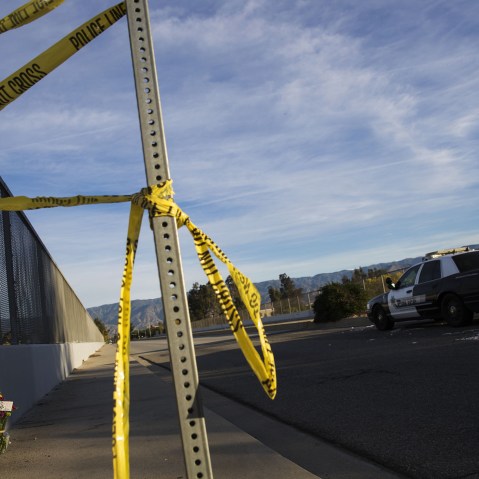 A San Bernardino police officer stands on the perimeter as crime scene tape and flowers rest near the Inland Regional Center on Dec. 3, 2015 in San Bernardino, Calif. (Photo by Patrick T. Fallon/AFP/Getty)