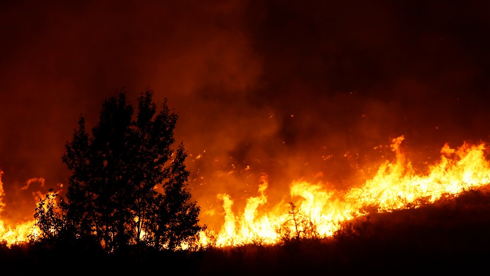 Flames rise near a tree on the ridge line above several homes on Twisp River Road just after midnight, Aug. 20, 2015 in Twisp, Wash. (Photo by Ted S. Warren/AP)