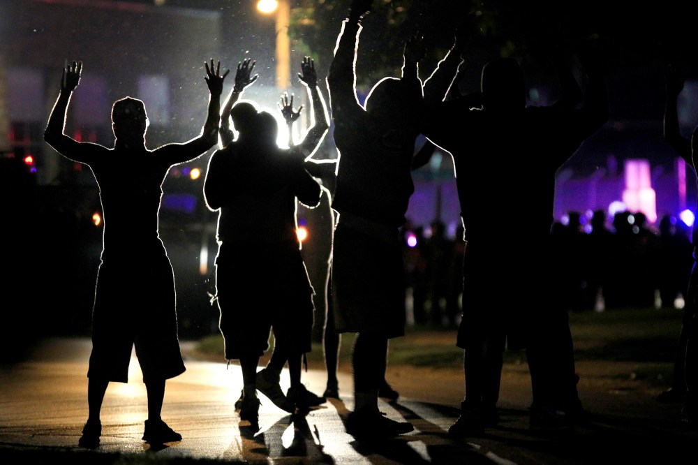 People raise their hands in the middle of the street as police wearing riot gear move toward their position trying to get them to disperse, Ferguson, Mo., Aug. 11, 2014. (Photo by Jeff Roberson/AP)