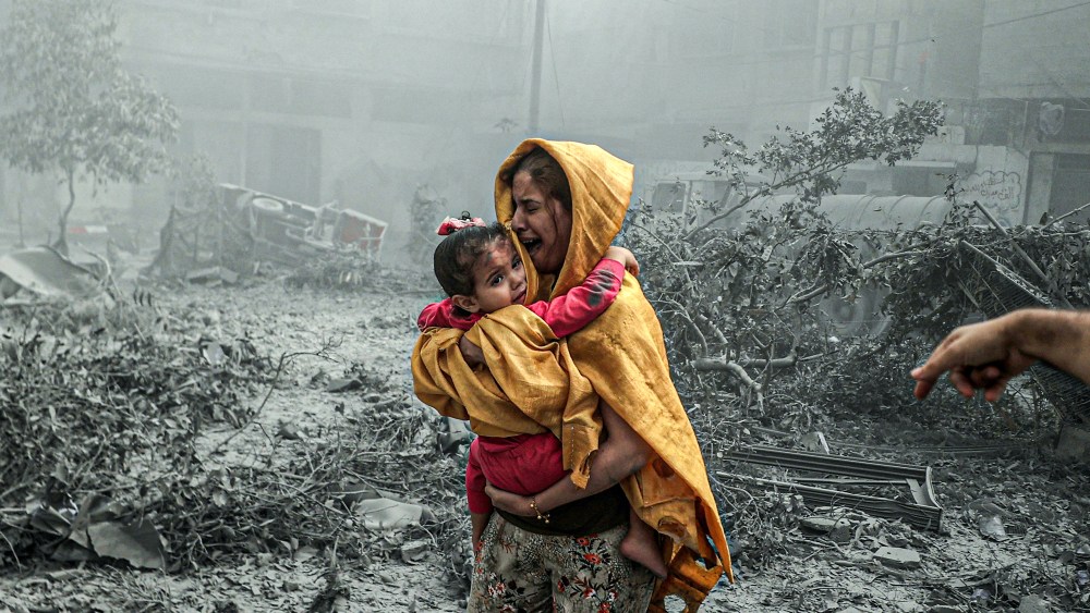 A woman holding a girl reacts after Israeli airstrikes hit