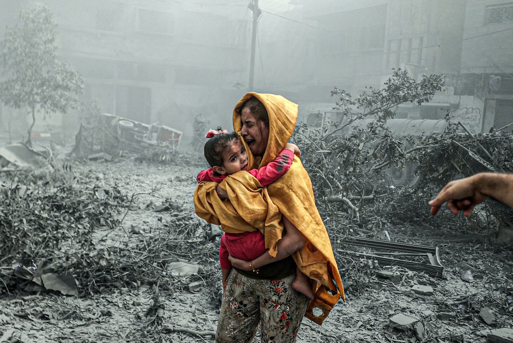 A woman holding a girl reacts after Israeli airstrikes hit
