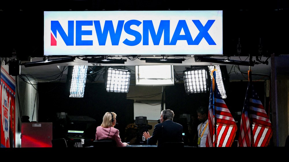 News anchors work at Newsmax's booth.