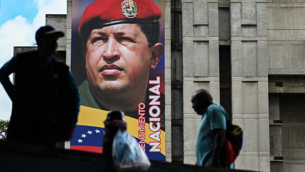 People walk past a mural of Hugo Chavez on the side of a building outside