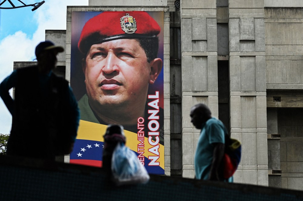People walk past a mural of Hugo Chavez on the side of a building outside
