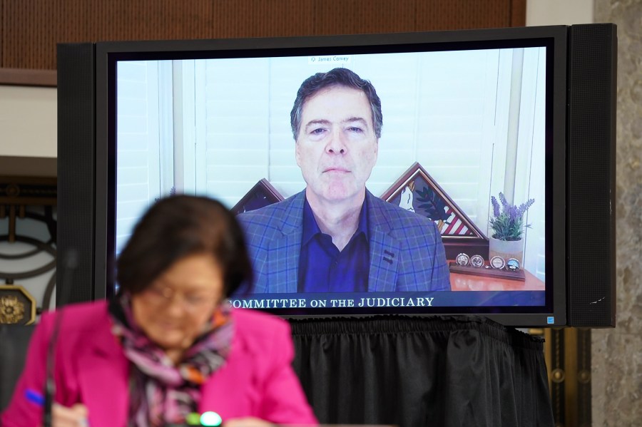 James Comey is seen on a video screen inside of a room