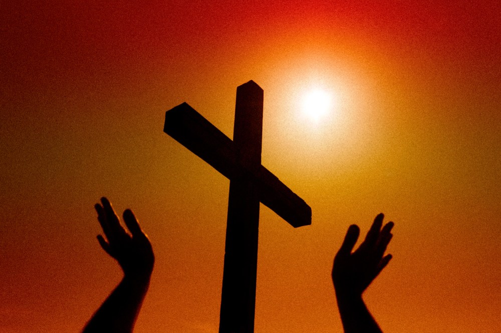 Silhouetted hands raised towards a bright sun and a wooden cross.