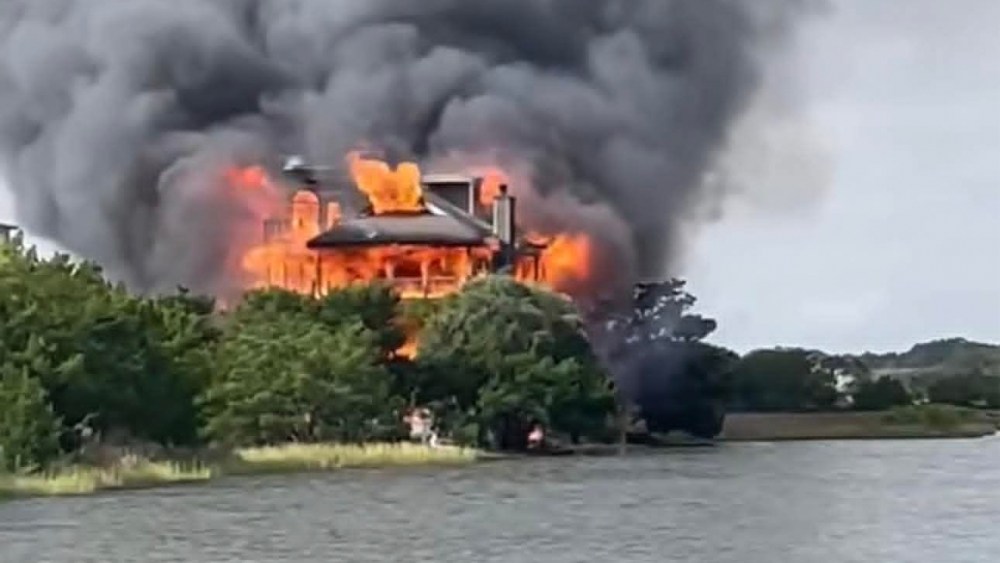 A view of a home on fire near a body of water.