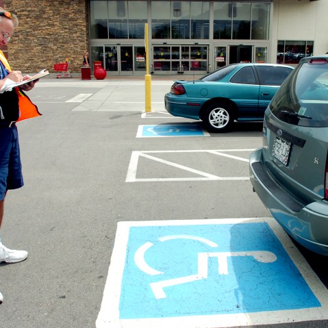 Volunteer handicapped parking enforcement officer writes a parking ticket for a car parked without a handicapped plate or place card.