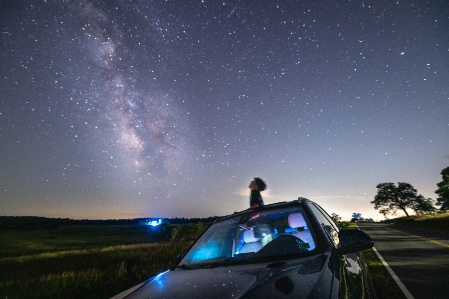 Teenage boy peeks out of car sunroof looking at the stars