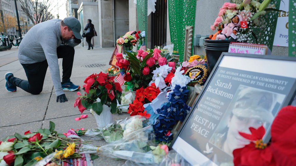 A jogger stops to pray at a makeshift memorial of flowers and American flags outside the Farragut West Metro station on Dec. 1, 2025, in Washington, D.C.
