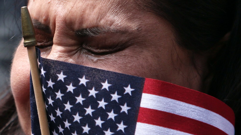 A woman tears up with a small American flag obscuring part of her face.