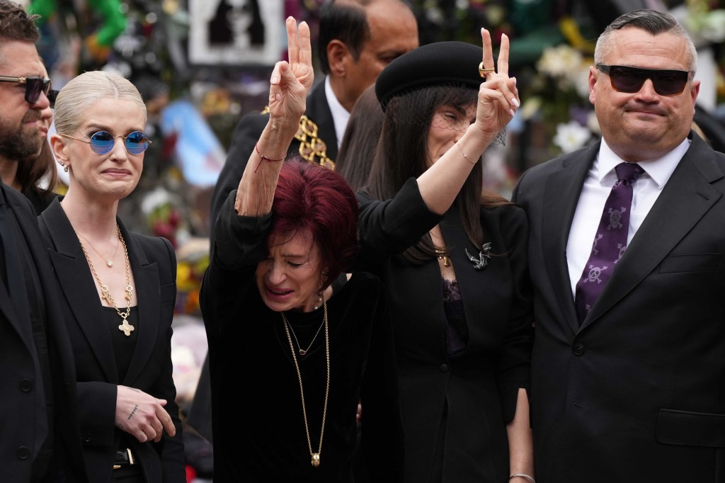 Sharon Osbourne holds up two peace signs while bowing her head during the funeral ceremony of her late husband, Ozzy Osbourne.