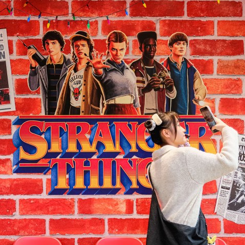 A person takes a photo by a wall embellished with Stranger Things decor.