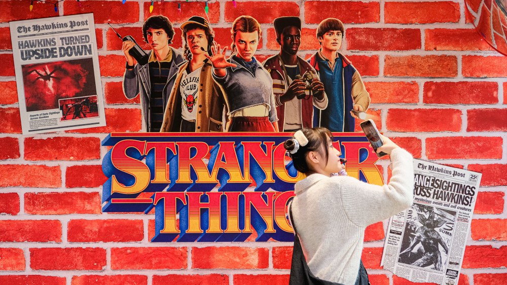 A person takes a photo by a wall embellished with Stranger Things decor.
