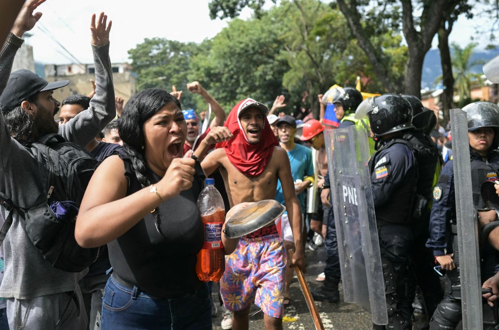 An anti-Maduro protestor bangs on a pan in front of police in Caracas after their election in the summer of 2024.
