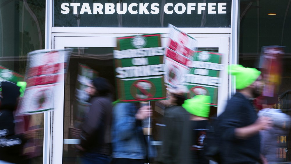 People blurred in motion hold signs in front of a Starbucks Coffee location.