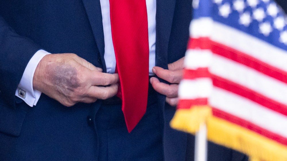 A close-up of Donald Trump’s right hand is seen as he buttons his jacket behind an American flag.