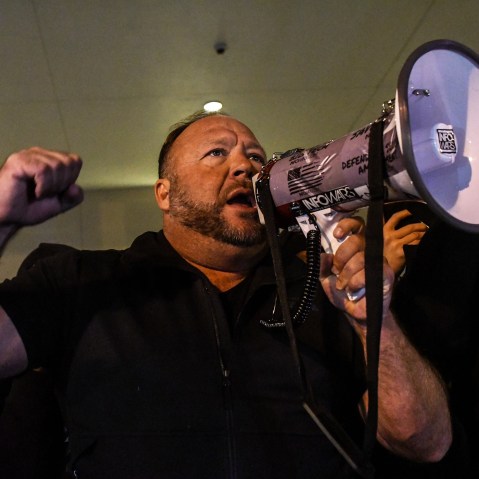 Alex Jones has one fist raised and holds a megaphone with the other hand.