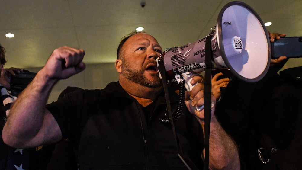 Alex Jones has one fist raised and holds a megaphone with the other hand.