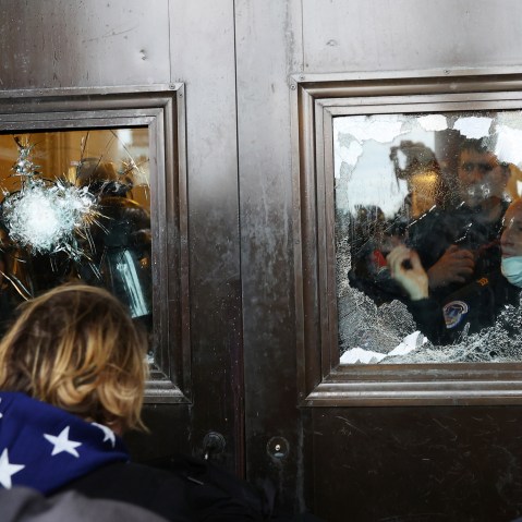 Police officer looks through a broken glass window as protesters stand outside.