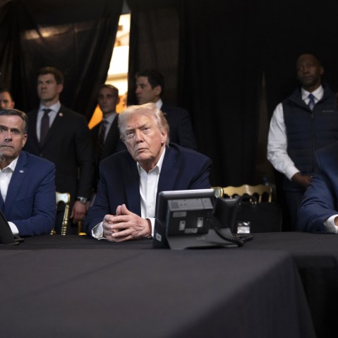 President Donald Trump, center, sits with his hands folded.