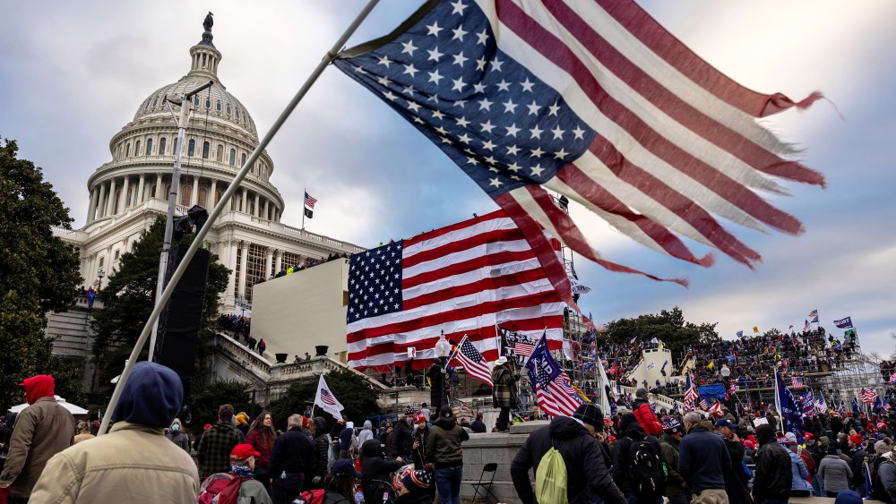 People, many with American flags, surround the Capitol.