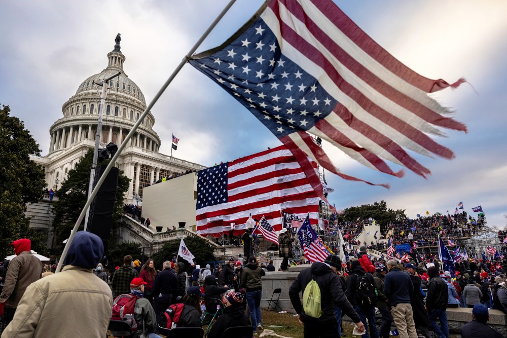 People, many with American flags, surround the Capitol.