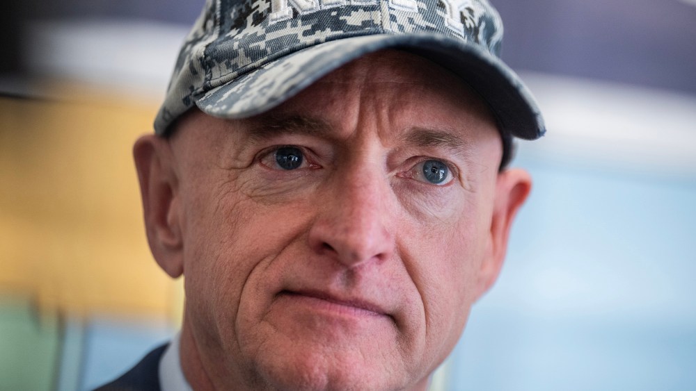 Arizona Sen. Mark Kelly looks on at an event, wearing a Navy cap.