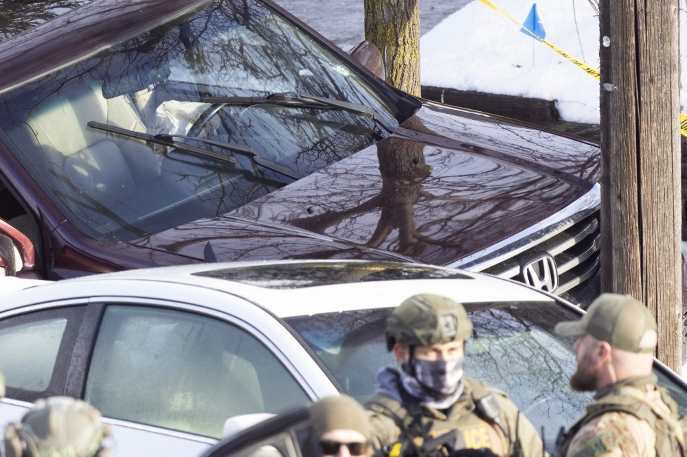 ICE agents next to a car crashed into a post.