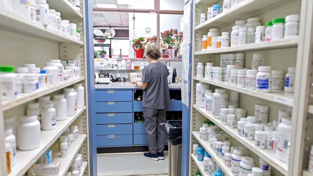 A pharmacy employee faces away from the camera by shelves with prescription drugs.