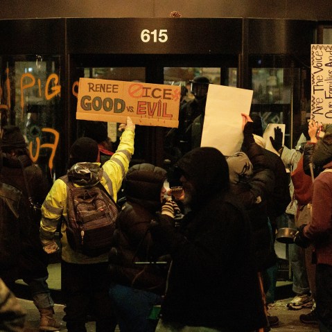 Protesters holding signs in front of Graduate Hotel in Minneapolis. There are some writings on the hotel windows, insulting ICE agents.