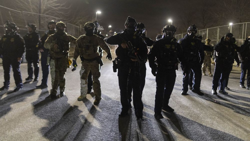 A line of ICE agents with guns drawn at nighttime.
