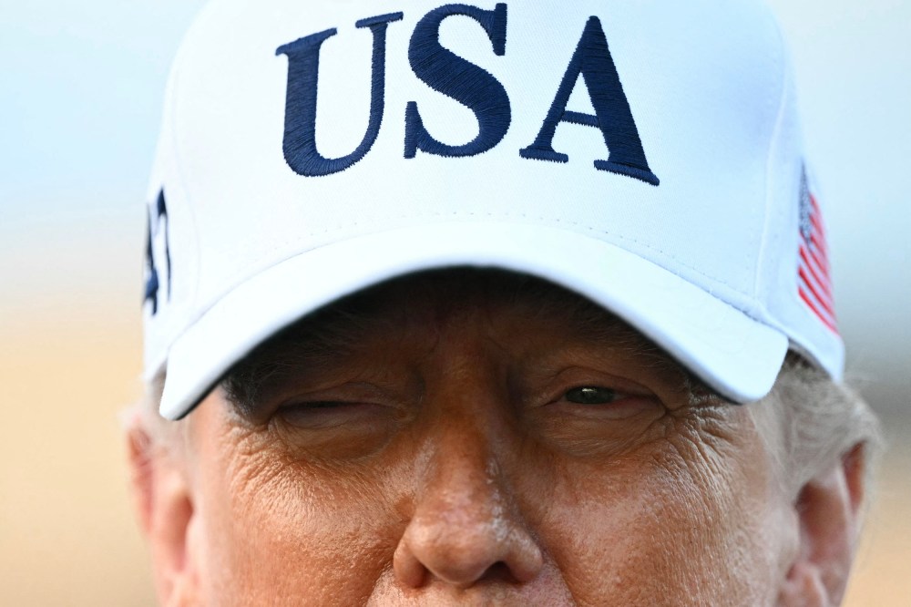 A closeup photo of President Trump shows the upper half of his face wearing a white USA hat.