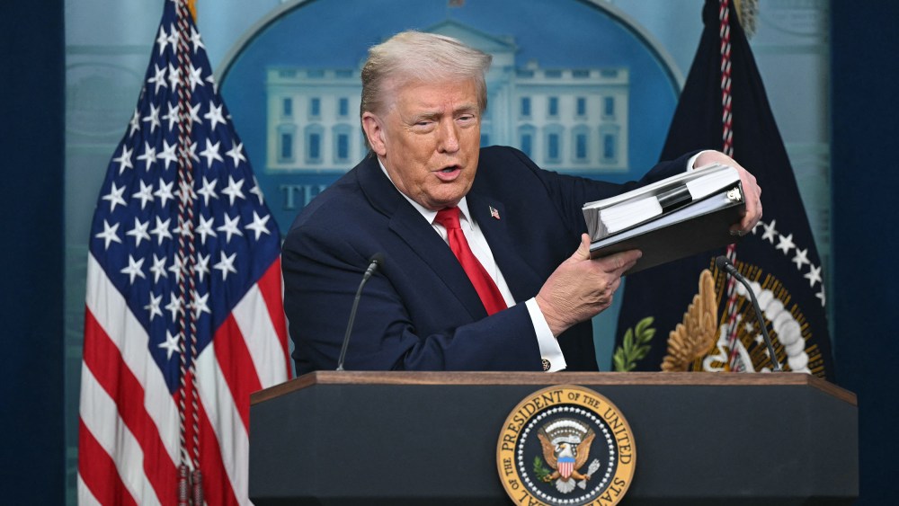 President Trump holds up a folder of documents as he speaks to the media during a briefing.