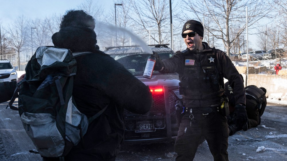 An officer sprays a protester with irritant gas in front of a police car.