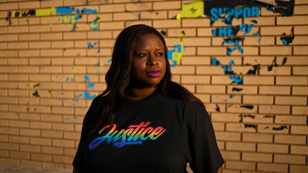 Nekima Levy Armstrong, wearing a shirt that says "justice" in rainbow letters, poses in front of a brick wall.