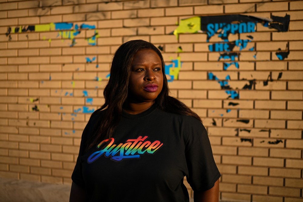 Nekima Levy Armstrong, wearing a shirt that says "justice" in rainbow letters, poses in front of a brick wall.