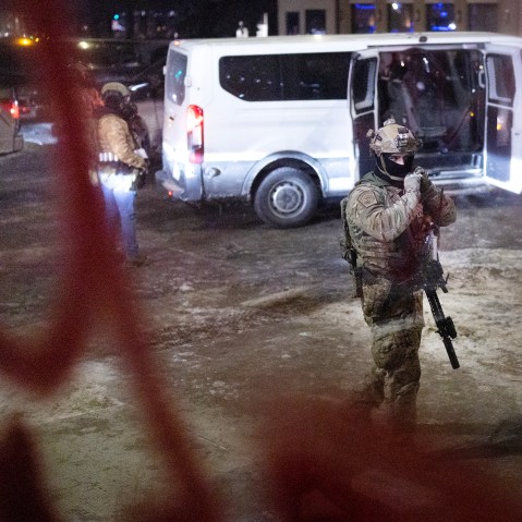 Several federal agents and their van are seen through a window at night.
