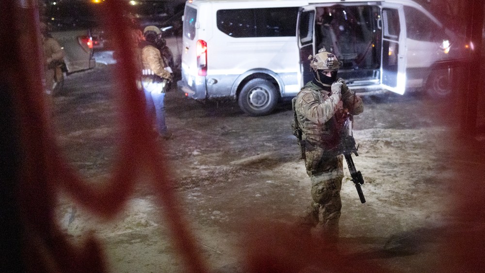 Several federal agents and their van are seen through a window at night.