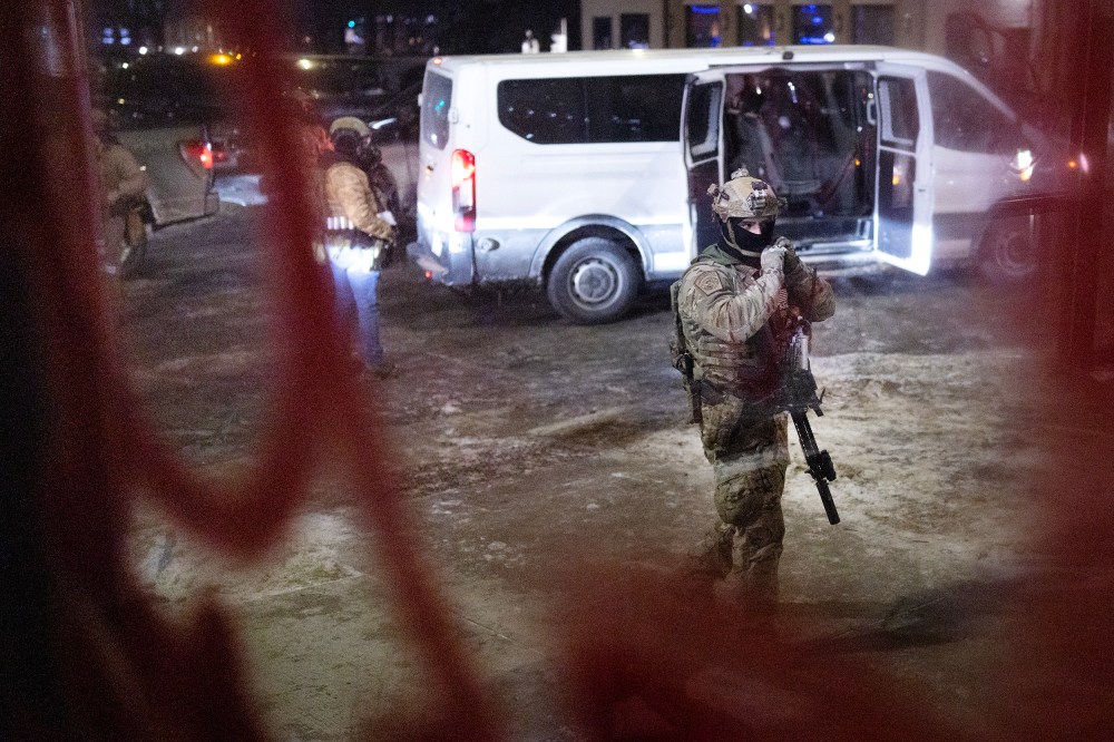 Several federal agents and their van are seen through a window at night.