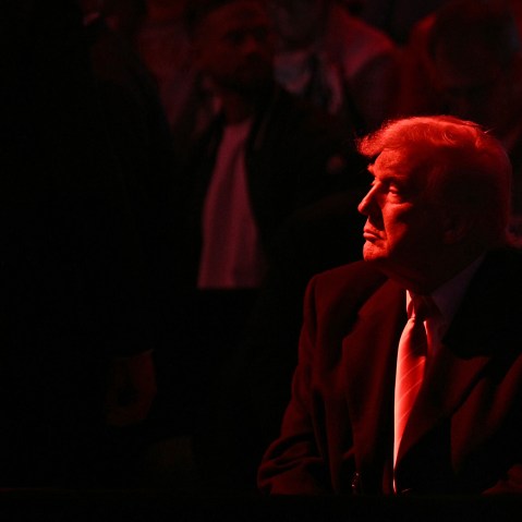 Donald Trump looks into the distance. He and the crowd are basked in red light.