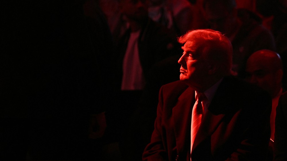 Donald Trump looks into the distance. He and the crowd are basked in red light.