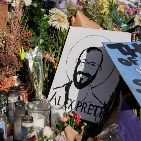 A memorial includes a drawing of Alex Pretti along with flowers and candles.