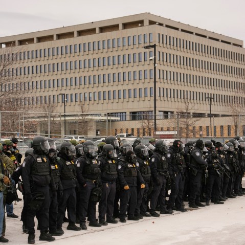 A crowd of federal immigration officers in helmets stand outside the Whipple Federal Building.