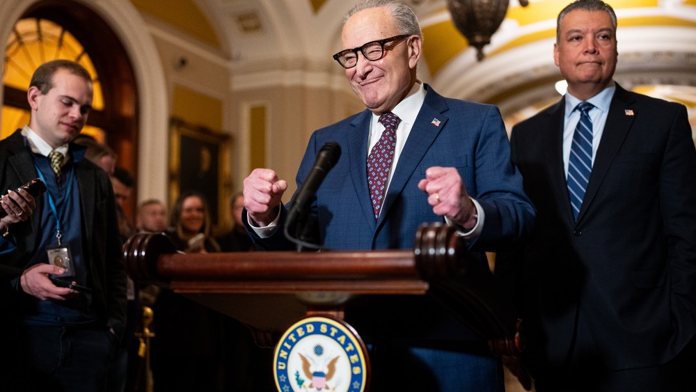 Chuck Schumer pumps his fists in excitement behind a podium.