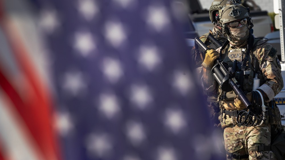 Federal law enforcement agents, right, with an American flag out of focus in the foreground.