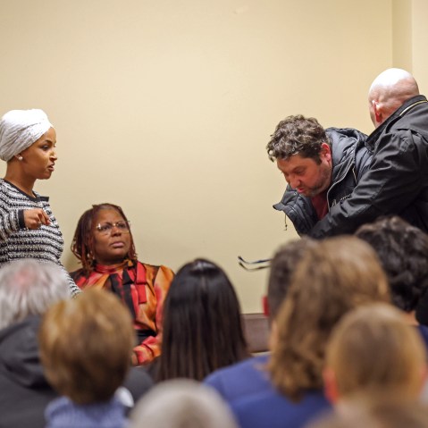 Ilhan Omar, left, raises her fist as if to throw a punch while security tackles a person from behind.