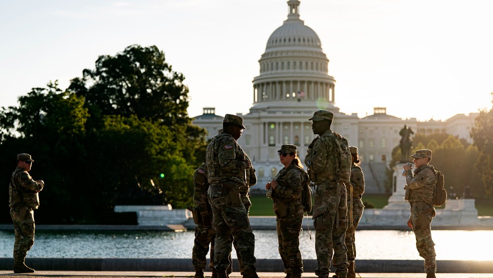 Several National Guard members stand by a pond across from the Capitol at sunset.