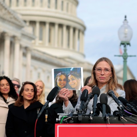 A woman standing at a lectern holds up a printed photograph in front of a crowd of other women.
